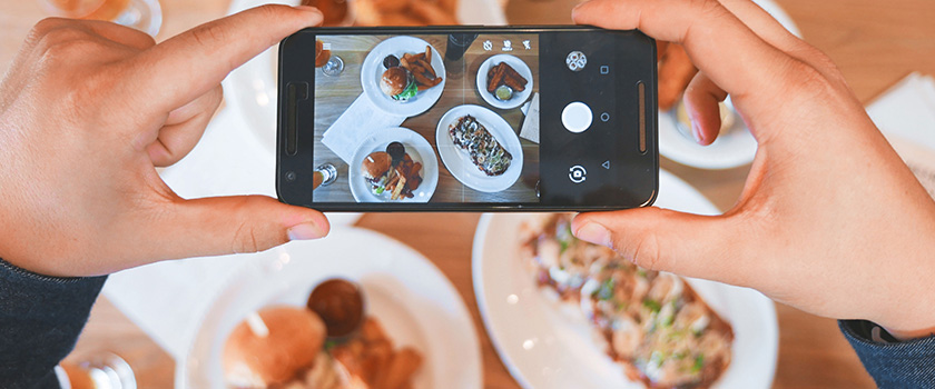 Phone hovered over table, taking photo of food